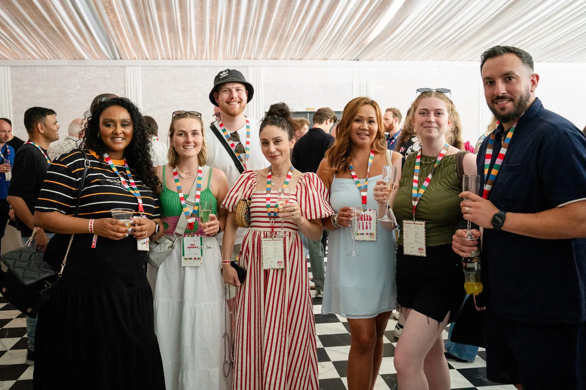 Seven people wearing Breadfest lanyards smile at the camera at an indoor event, drinks in hand.