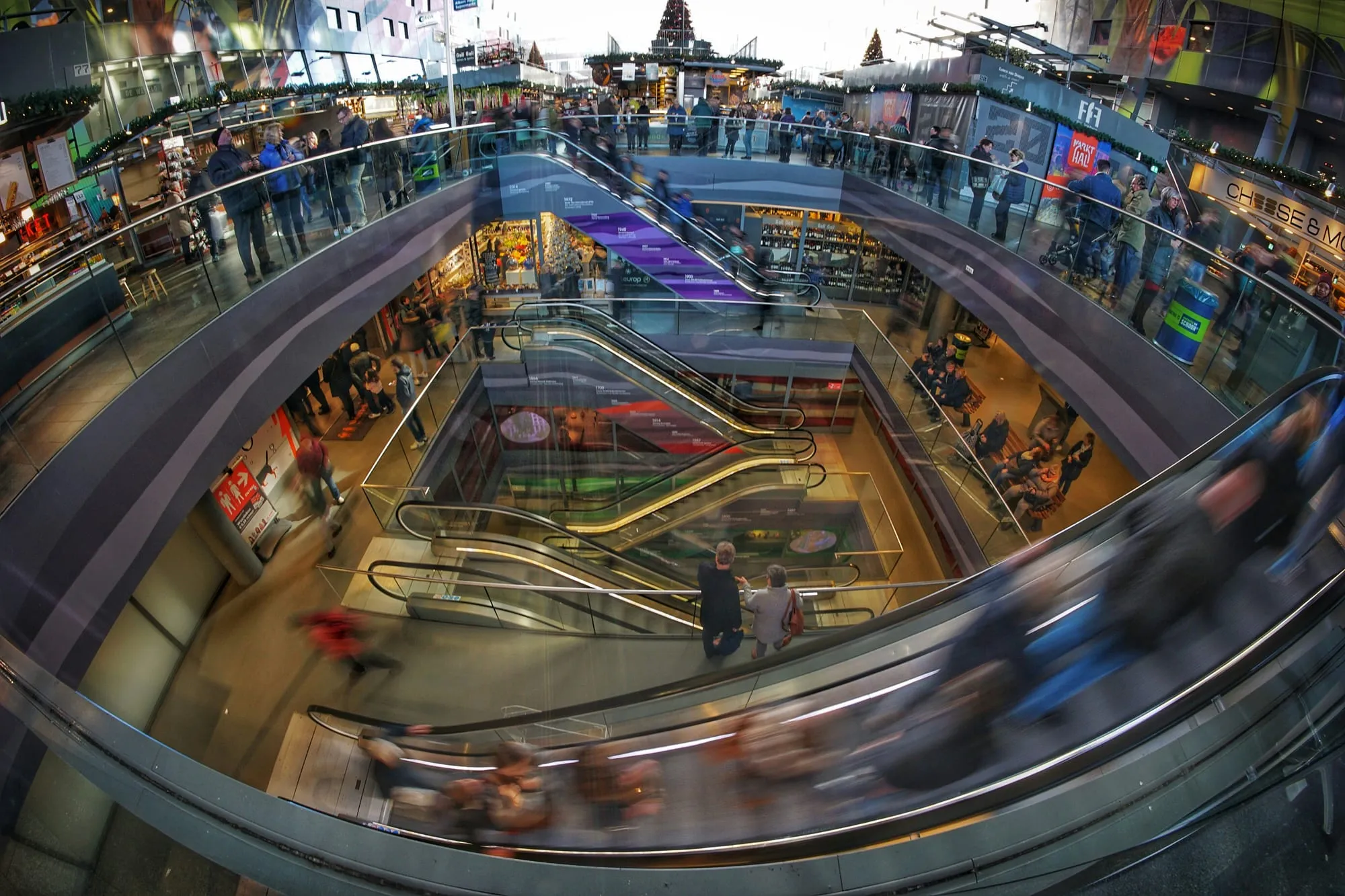 Shoppers on escalators and walkways inside a busy multi-level indoor market.